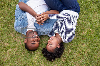 Young black couple lying on grass look at each other, aerial