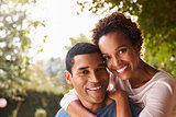 Young black couple piggyback in garden looking at camera