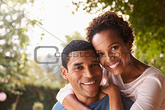 Young black couple piggyback in garden looking at camera