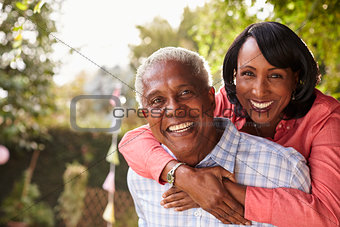 Senior black couple piggyback in garden looking at camera