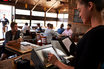 Young woman preparing bill at restaurant using touch screen