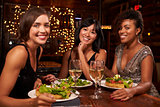 Three female friends at dinner in restaurant look to camera