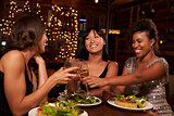 Three female friends make a toast over dinner at restaurant