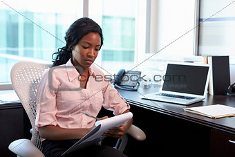Female Doctor Sitting At Desk In Office Making Notes