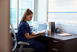 Nurse Wearing Scrubs Working At Desk In Office
