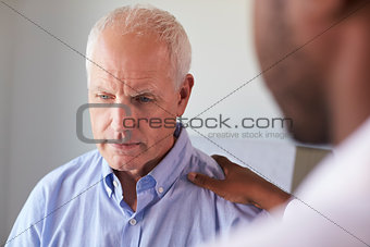 Doctor Talking To Unhappy Male Patient In Exam Room