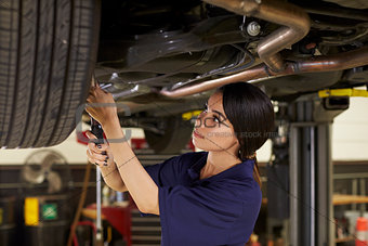 Female Auto Mechanic Working Underneath Car In Garage