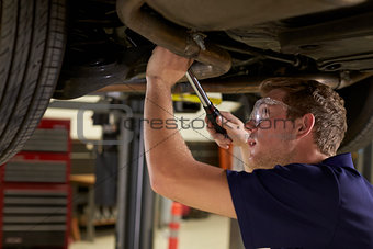 Auto Mechanic Working Underneath Car In Garage