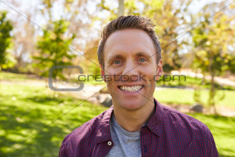 Happy white adult man in park looking to camera, close up