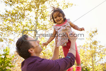 Father throwing his young daughter in the air in a park