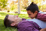 Mixed race Asian boy lying on top of his dad in a park