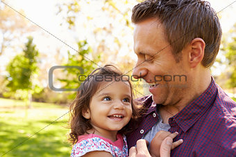 White dad holding his young mixed race daughter in a park