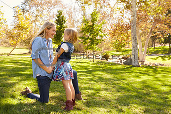 Mother and young daughter talking in a park, full length