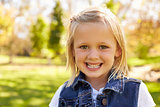 Five year old blonde girl in a park smiling to camera