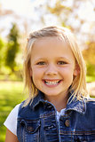 Five year old blonde girl in park smiles to camera, vertical