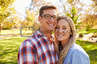 Adult Caucasian couple embracing in a park looking to camera