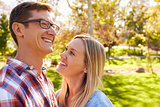 Adult Caucasian couple embracing in a park looking away