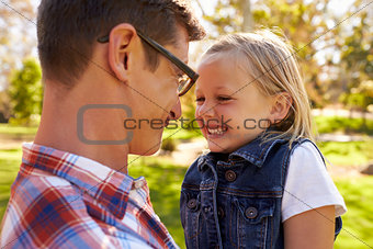 Dad and young daughter pulling faces at each other in a park