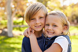 Young brother and sister embracing in a park look to camera
