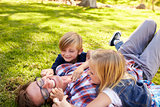Two kids playing with their dad, lying in a park, side view