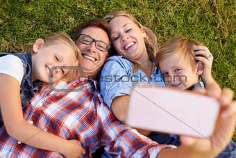 Young white family lying on grass in a park taking a selfie