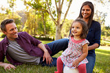 Mixed race parents and young daughter sit in park, close up