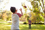 Dad and son throwing American football to each other in park