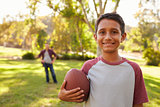 Portrait of boy holding football in park, dad in background