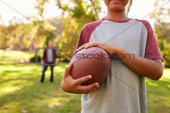 Boy holding football in park, crop, dad in background