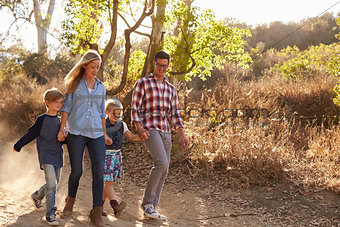 Young white family walking on a path in sunlight, front view