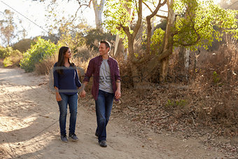 Mixed race couple walking in park holding hands, front view