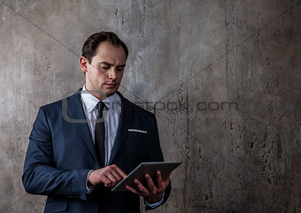 Portrait of a businessman with tablet on concrete gray wall background
