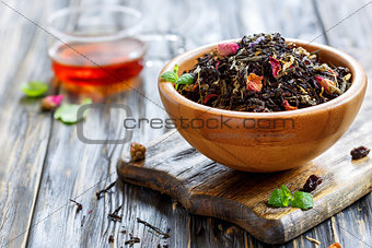 Wooden bowl with a black tea with flower petals.
