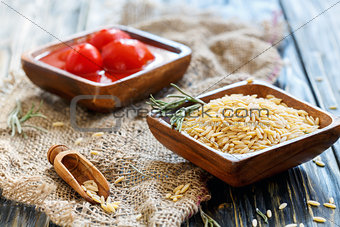 Wooden bowls with orzo pasta and canned tomatoes.