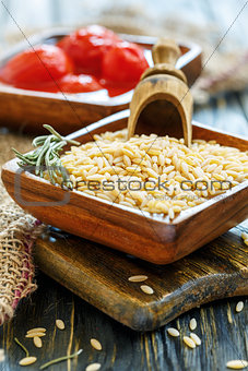 Orzo pasta and wooden scoop in bowl close-up.