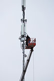 Two workers assemble equipment for telecommunications on the tower with the help of the lift in the winter