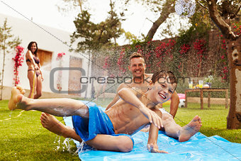 Family Having Fun On Water Slide In Garden