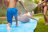 Rear View Of Family Having Fun On Water Slide In Garden