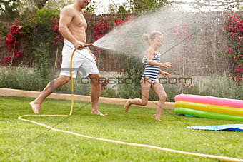 Father Spraying Daughter With Garden Hose