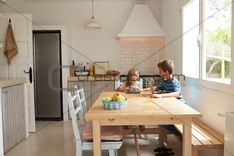 Children At Home Using Digital Devices On Kitchen Table