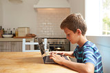 Boy At Home Using Laptop On Kitchen Table