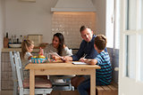 Parents Helping Children With Homework At Kitchen Table