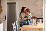 Son Sitting On Kitchen Table And Hugging Mother