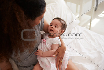Mother Cuddling Baby Daughter In Bedroom At Home