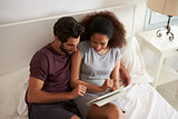 Couple Sitting On Bed Looking At Digital Tablet Together