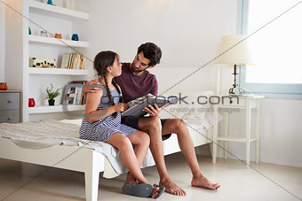 Father And Daughter Sitting On Bed Reading Book Together