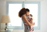 Mother Cuddling Baby Daughter At Home In Front Of Window