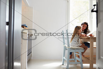 Mother And Daughter Sitting At Kitchen Table Reading Book