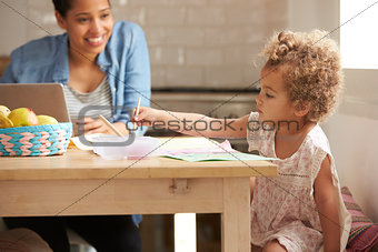 Girl Paints At Kitchen Table As Mother Works At Laptop
