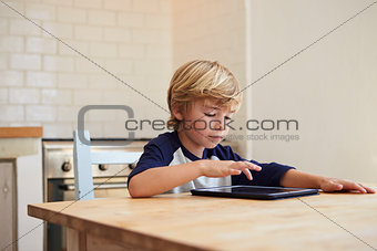 Young boy using tablet computer at kitchen table